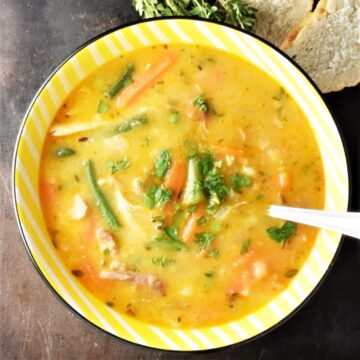 Top down view of leftover turkey soup with vegetables in yellow bowl.
