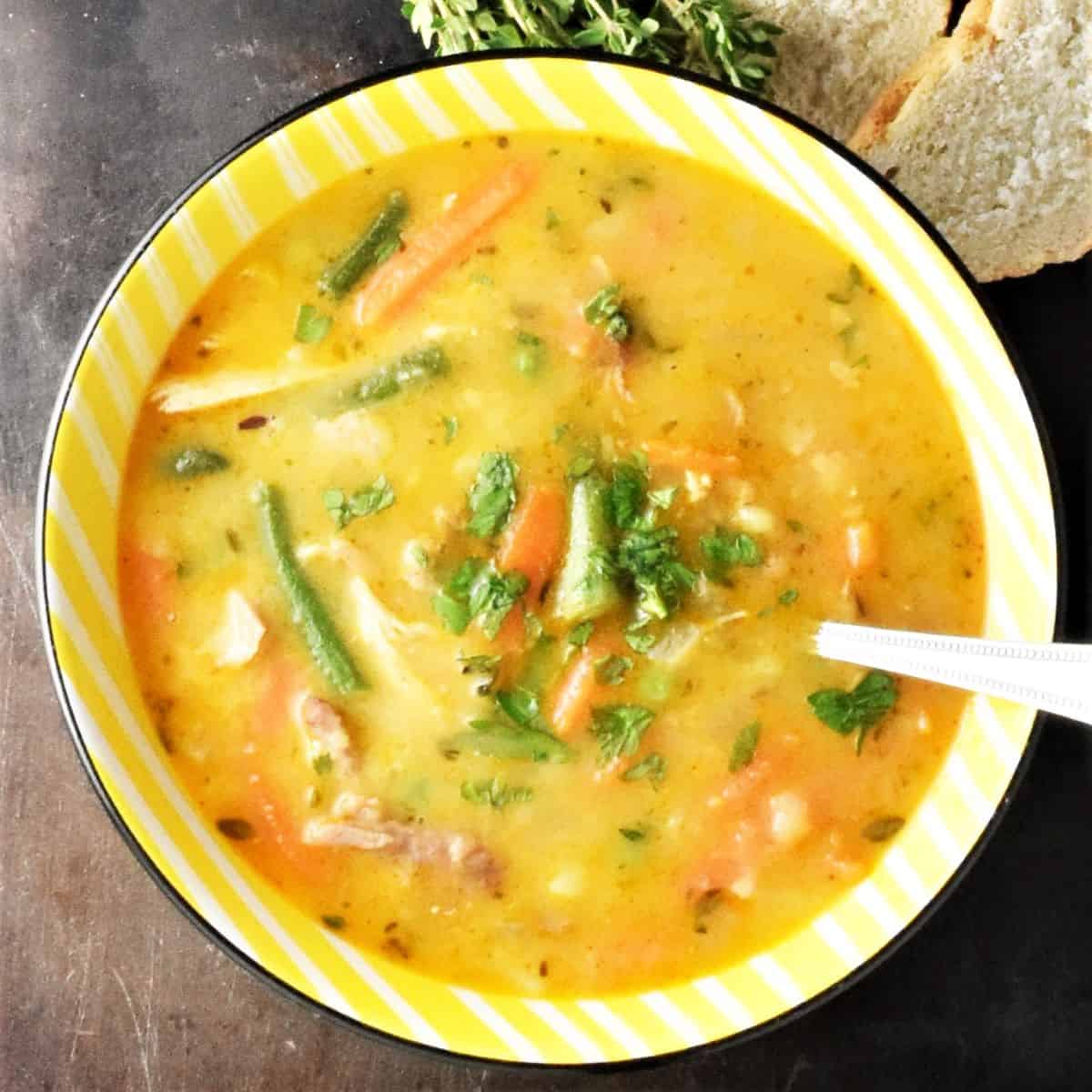 Top down view of leftover turkey soup with vegetables in yellow bowl.