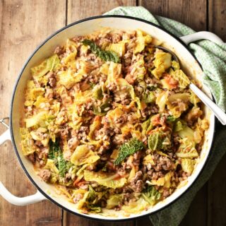 Cabbage, ground meat and rice in large shallow white dish with spoon and green cloth in top right corner.