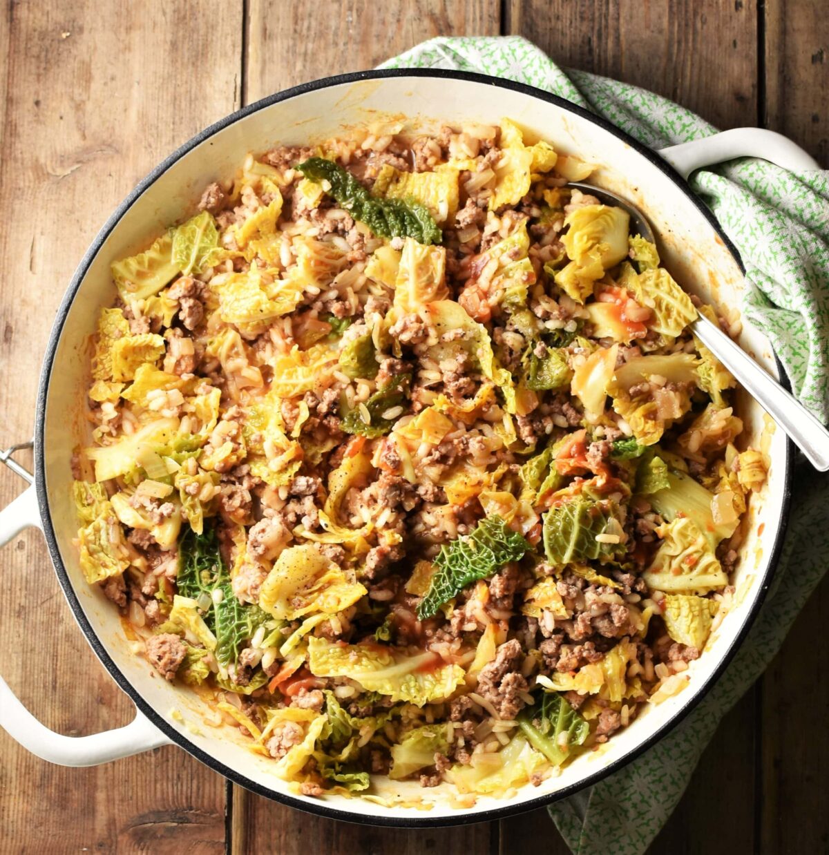 Cabbage, ground meat and rice in large shallow white dish with spoon and green cloth in top right corner.