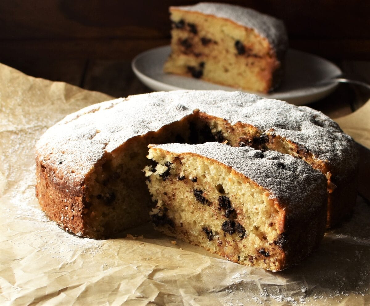 Side view of marzipan cake slice with cake in background on top of paper.
