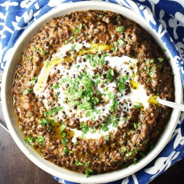 Top down view of black lentil curry in white bowl with spoon.