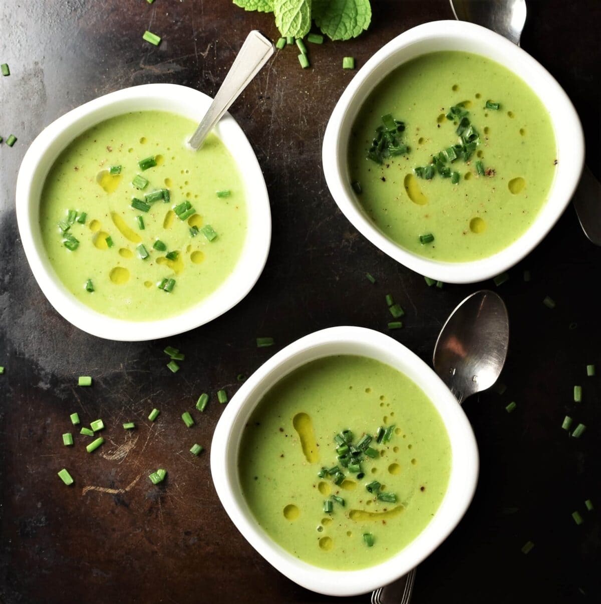 Top down view of creamy cucumber soup in 3 white bowls with spoons.