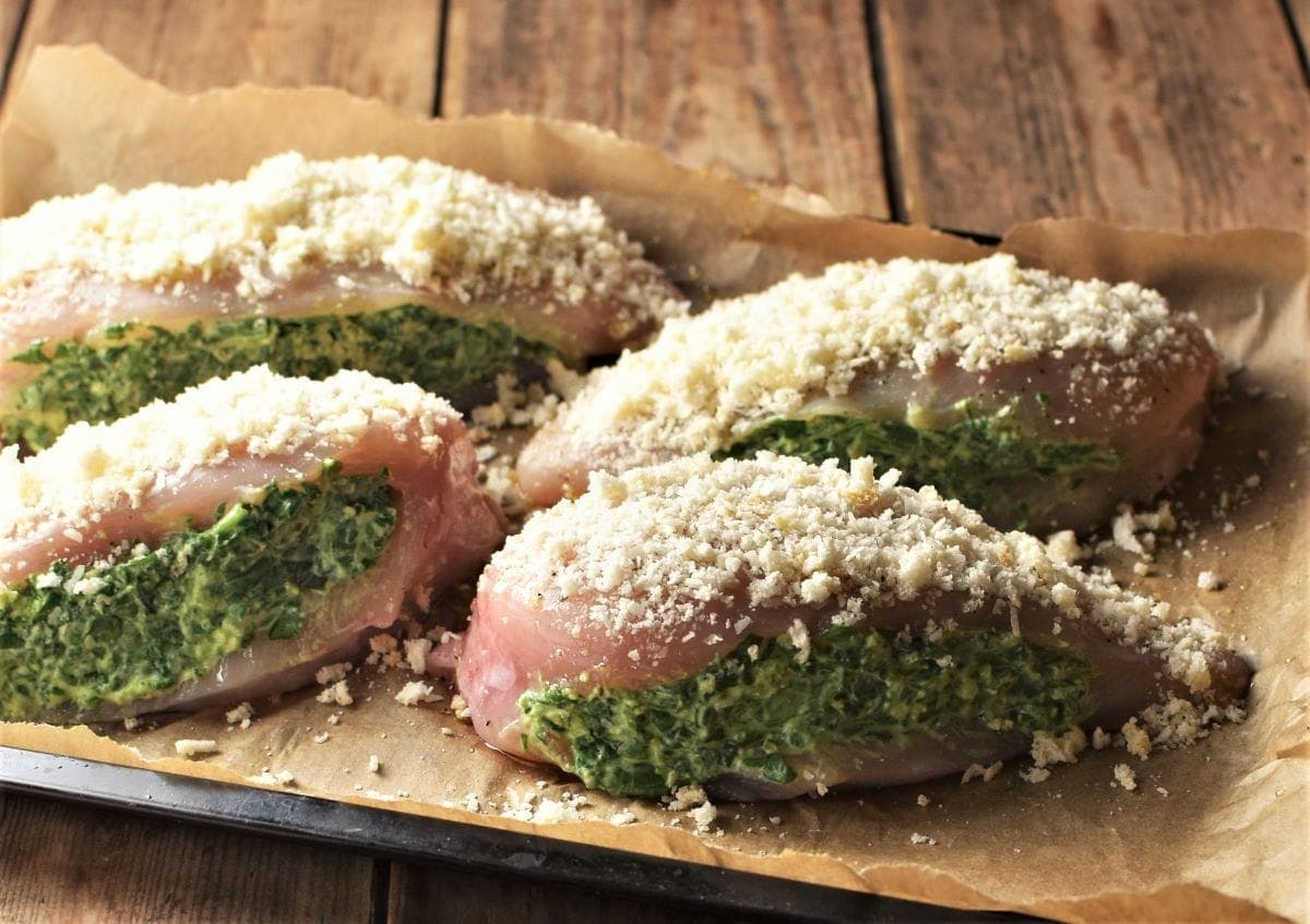 Side view of 4 unbaked spinach stuffed chicken breasts on top of parchment.