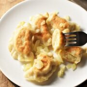 Vegan pierogi with onion and fork on white plate.