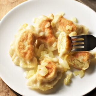 Vegan pierogi with onion and fork on white plate.