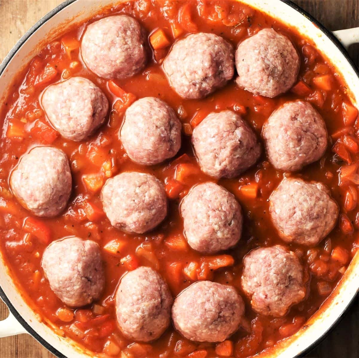 Raw meatballs in chunky tomato sauce in large pan.