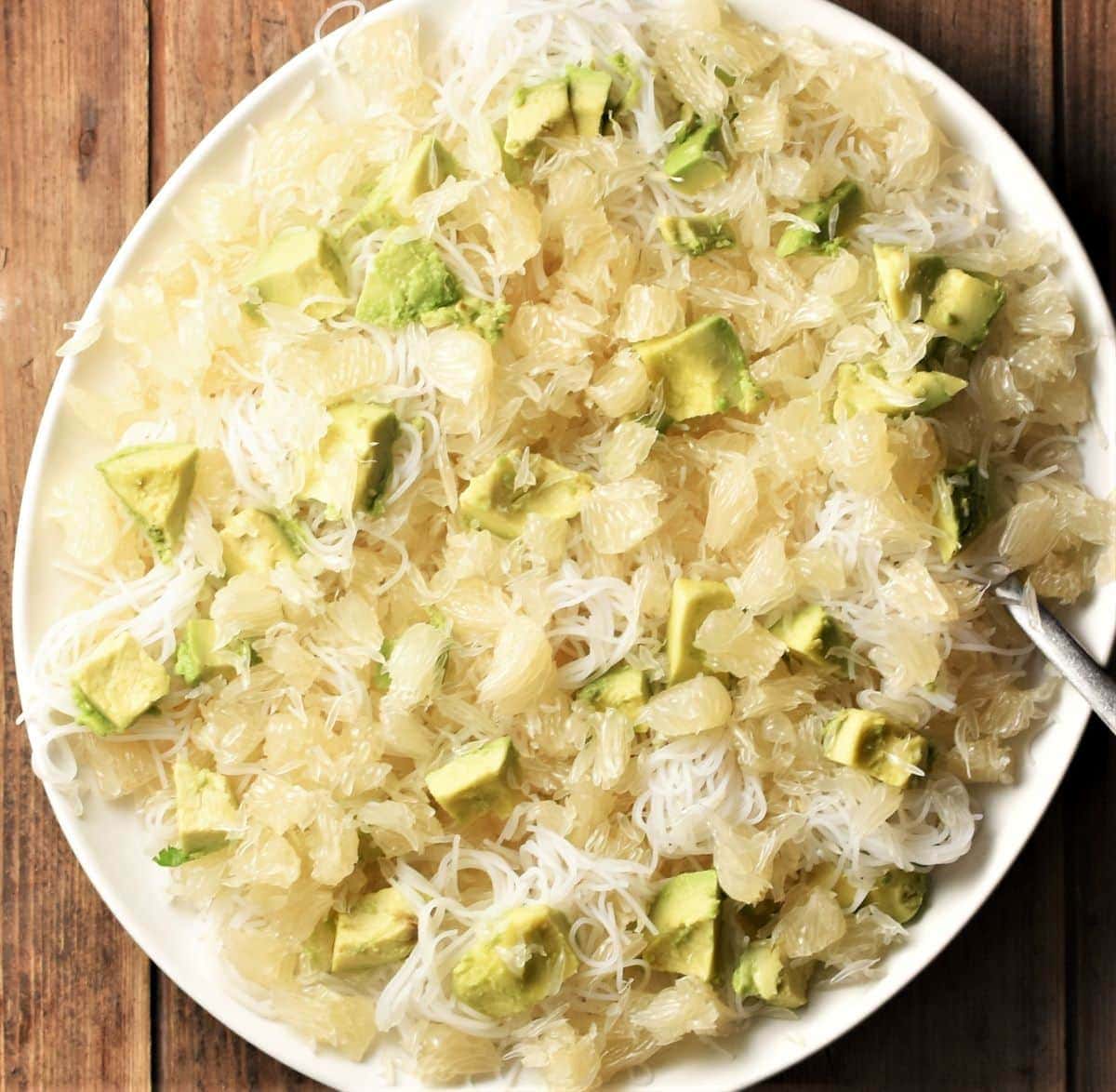 Assembling pomelo salad with noodles and avocado on plate.