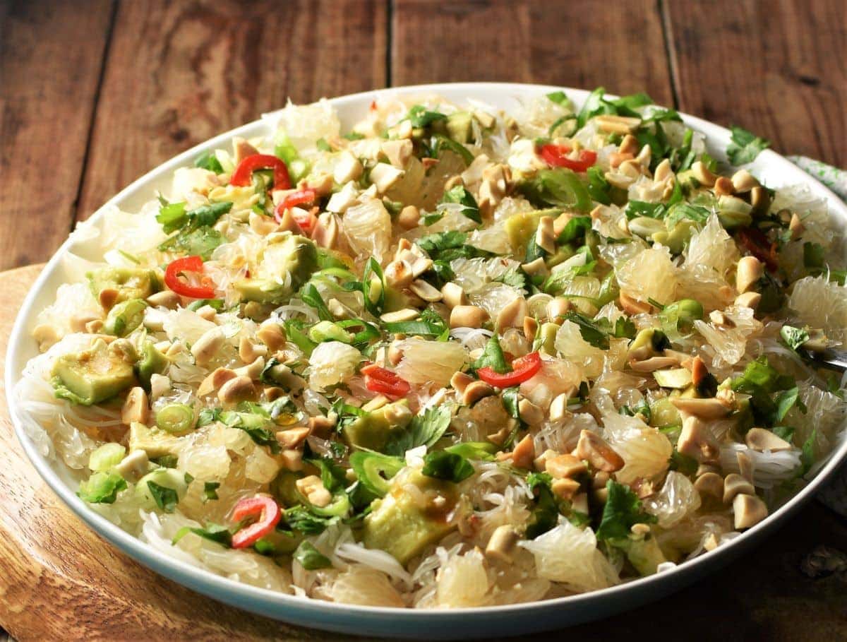 Side view of pomelo salad with noodles on large plate.