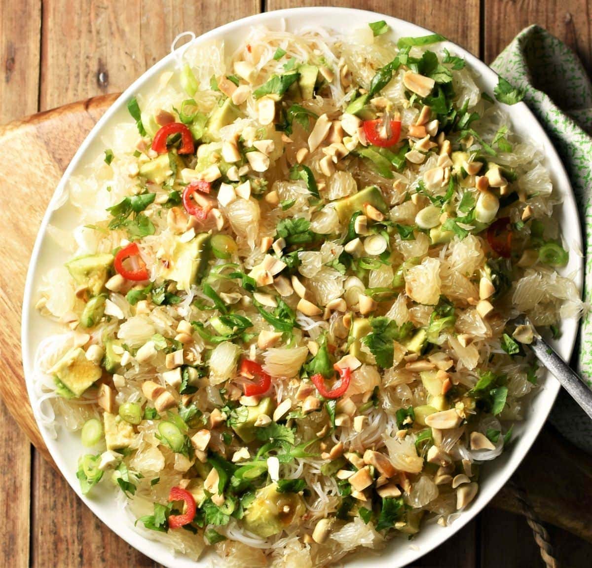 Top down view of pomelo salad with noodles, avocado and herbs on white plate.