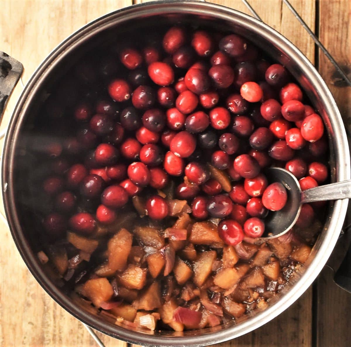 Cooking cranberries with apples and spices in pot.