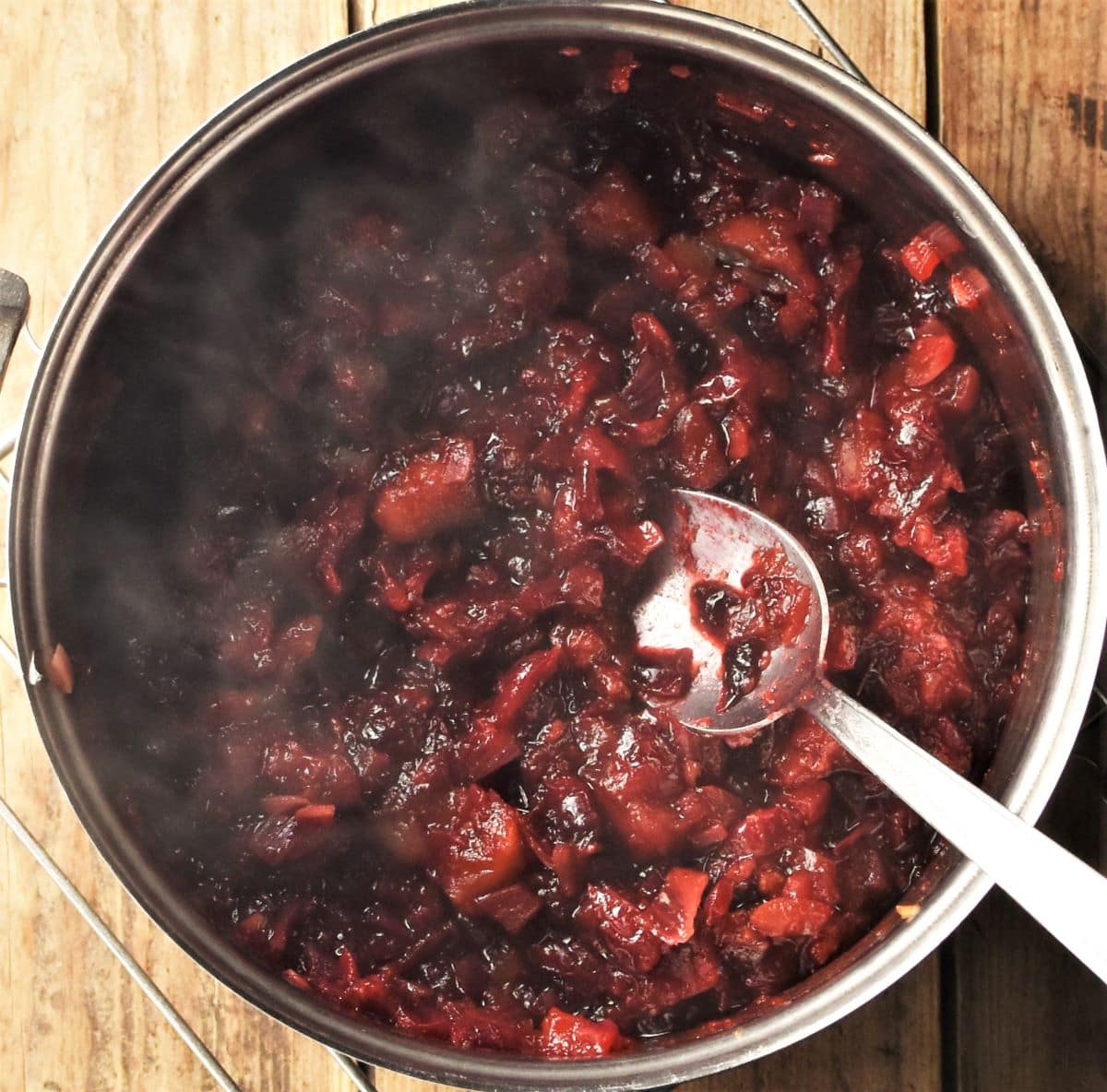 Cooking cranberry chutney in pot with spoon.