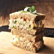 Side view of halved turkey salad sandwich stacked on top of cutting board.