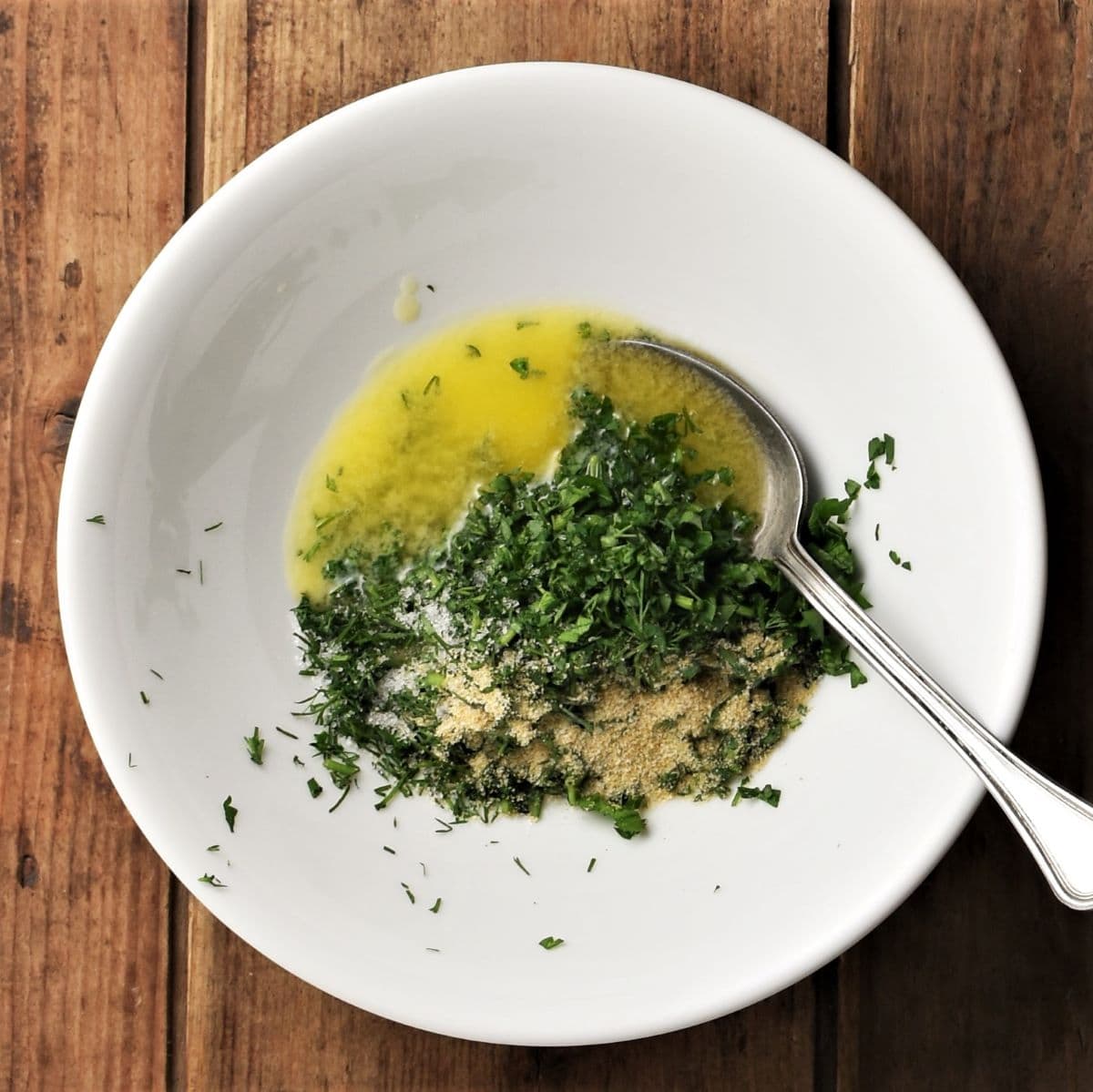 Fresh herbs with butter in white bowl with spoon.