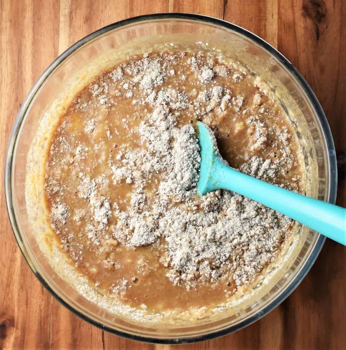 Making banana and peanut butter muffin batter in bowl with blue spoon.