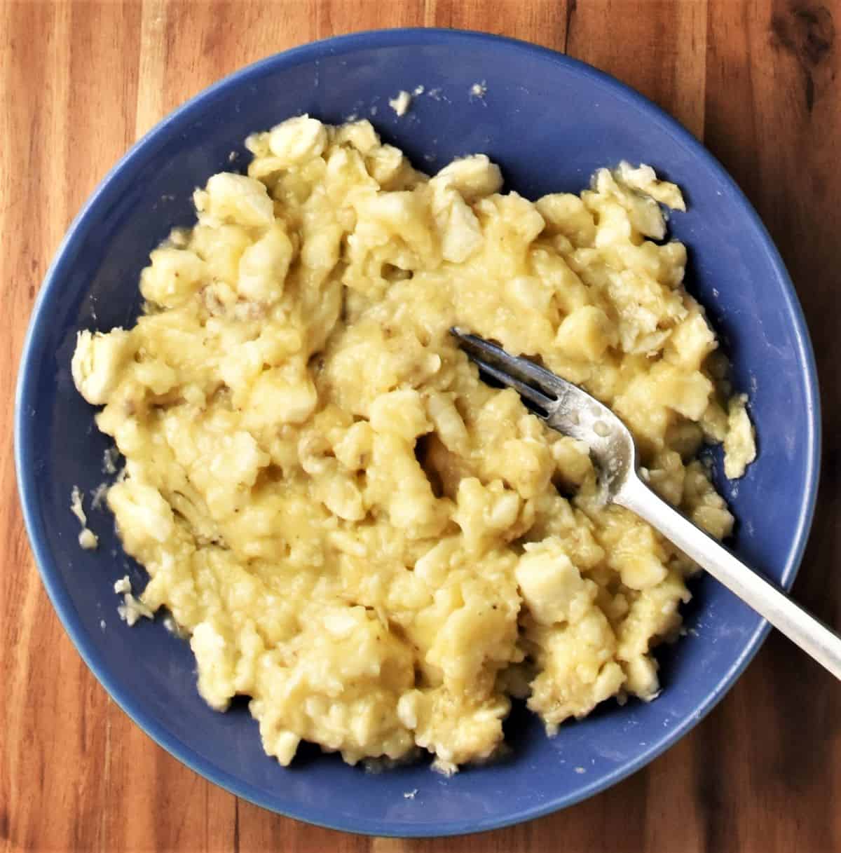 Partly mashed lumpy banana mixture with form in blue bowl.