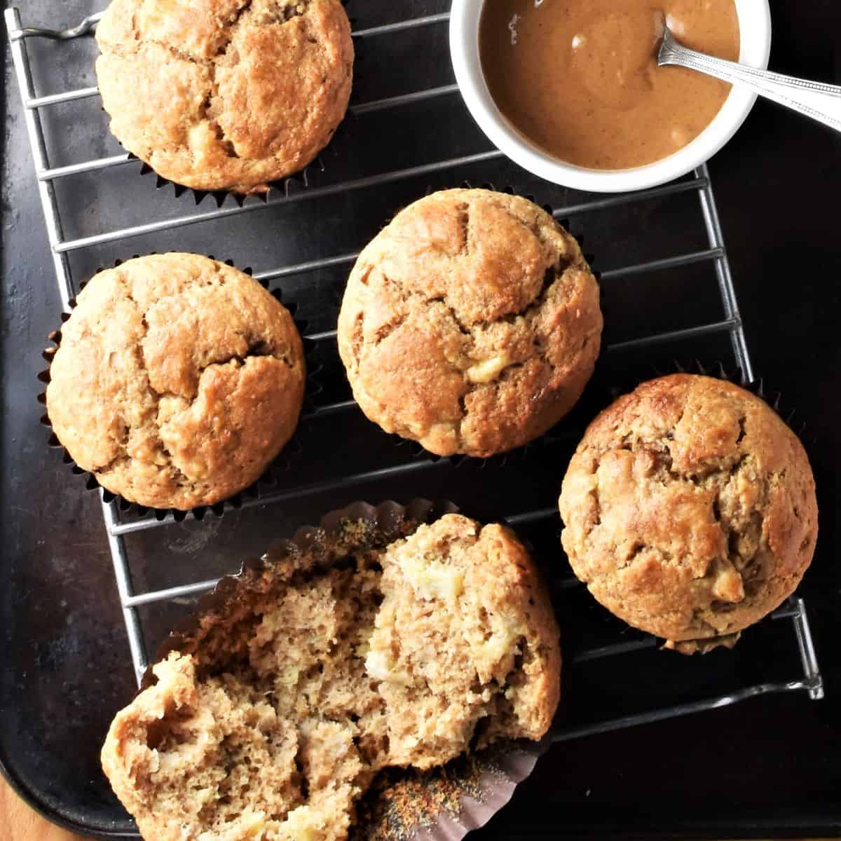 Top down view of peanut butter banana muffins on rack with peanut butter in bowl with spoon.