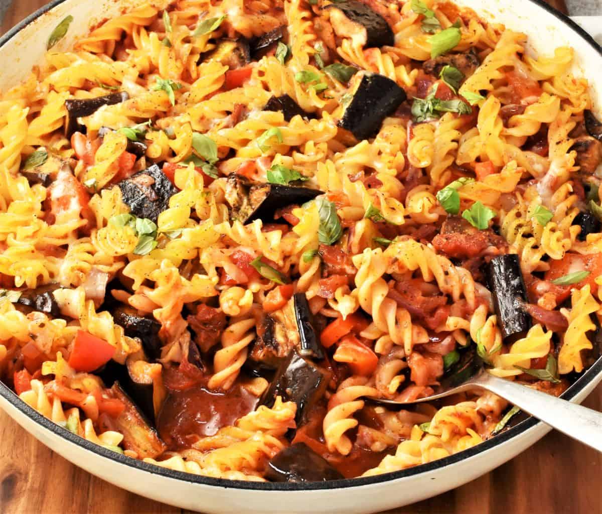 Side view of roasted eggplant and pasta bake in large shallow dish with spoon.