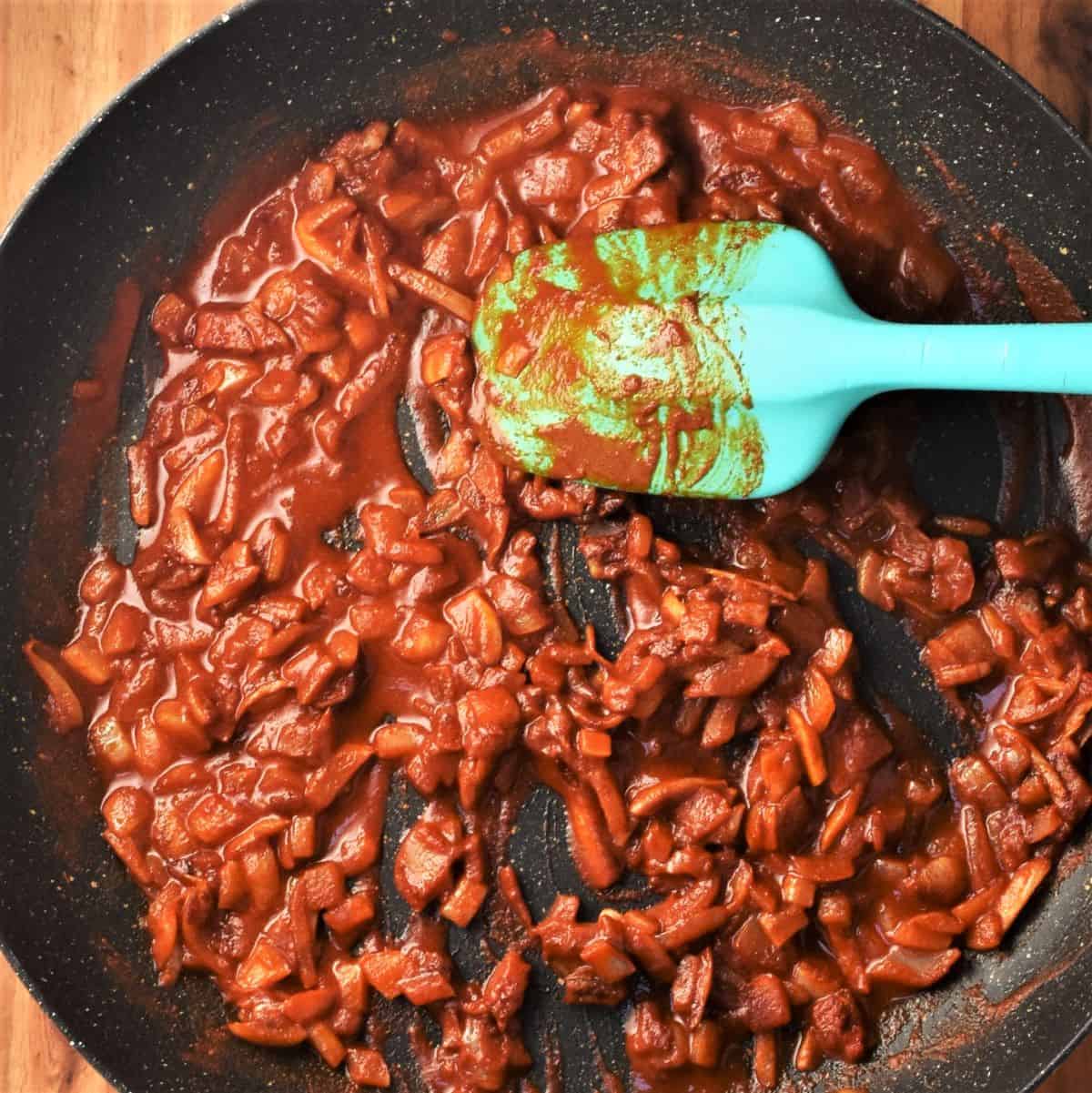 Chopped onion and paprika in large pan with blue spatula.