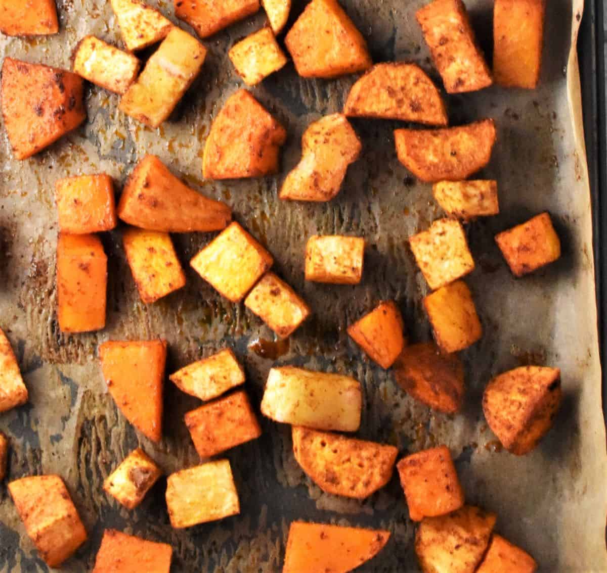 Roasted spiced vegetable pieces on top of baking sheet with parchment.