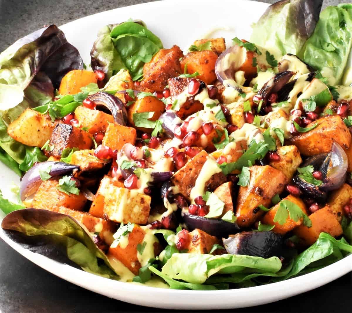 Side view of salad with roasted vegetables and creamy dressing .