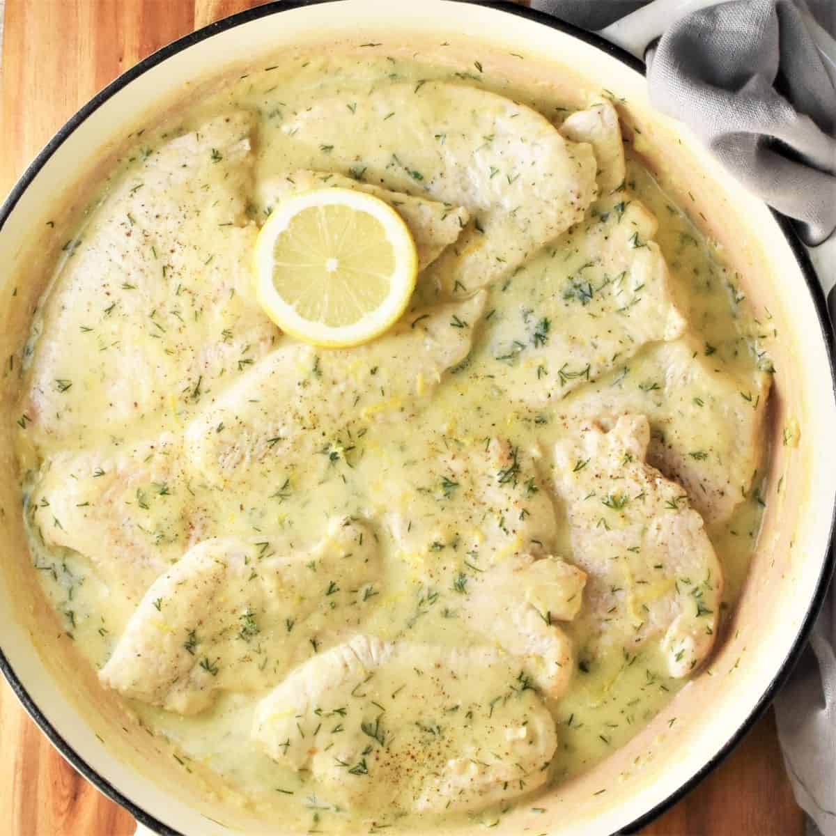 Top down view of turkey steaks in creamy sauce in large shallow pan.
