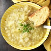 Top down view of chunky leek and cauliflower soup in yellow bowl with toast.