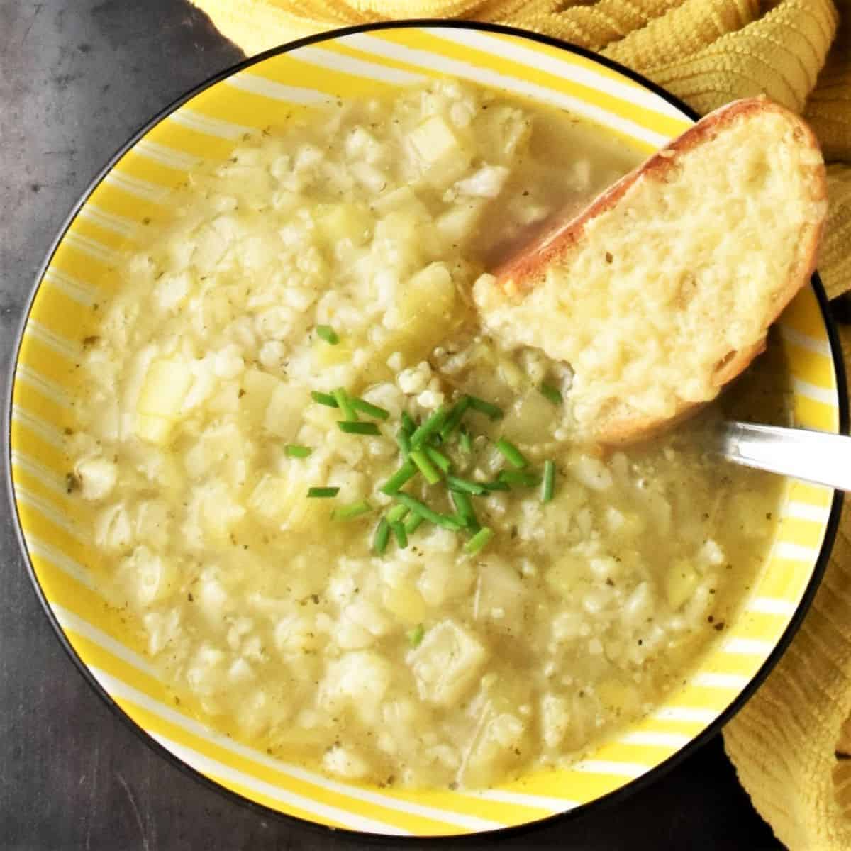 Top down view of chunky leek and cauliflower soup in yellow bowl with toast.