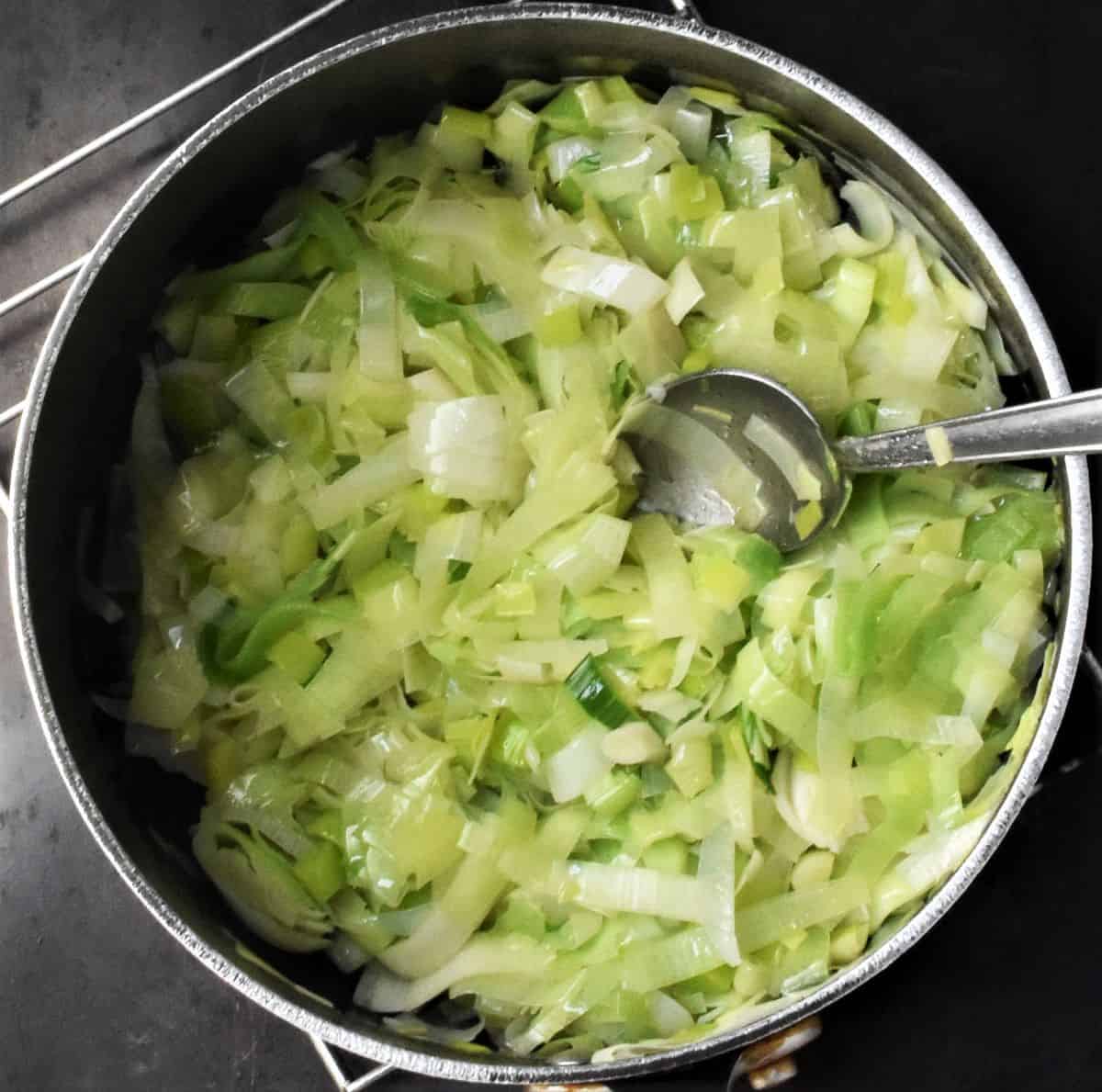 Cooking chopped leeks in pot with spoon.