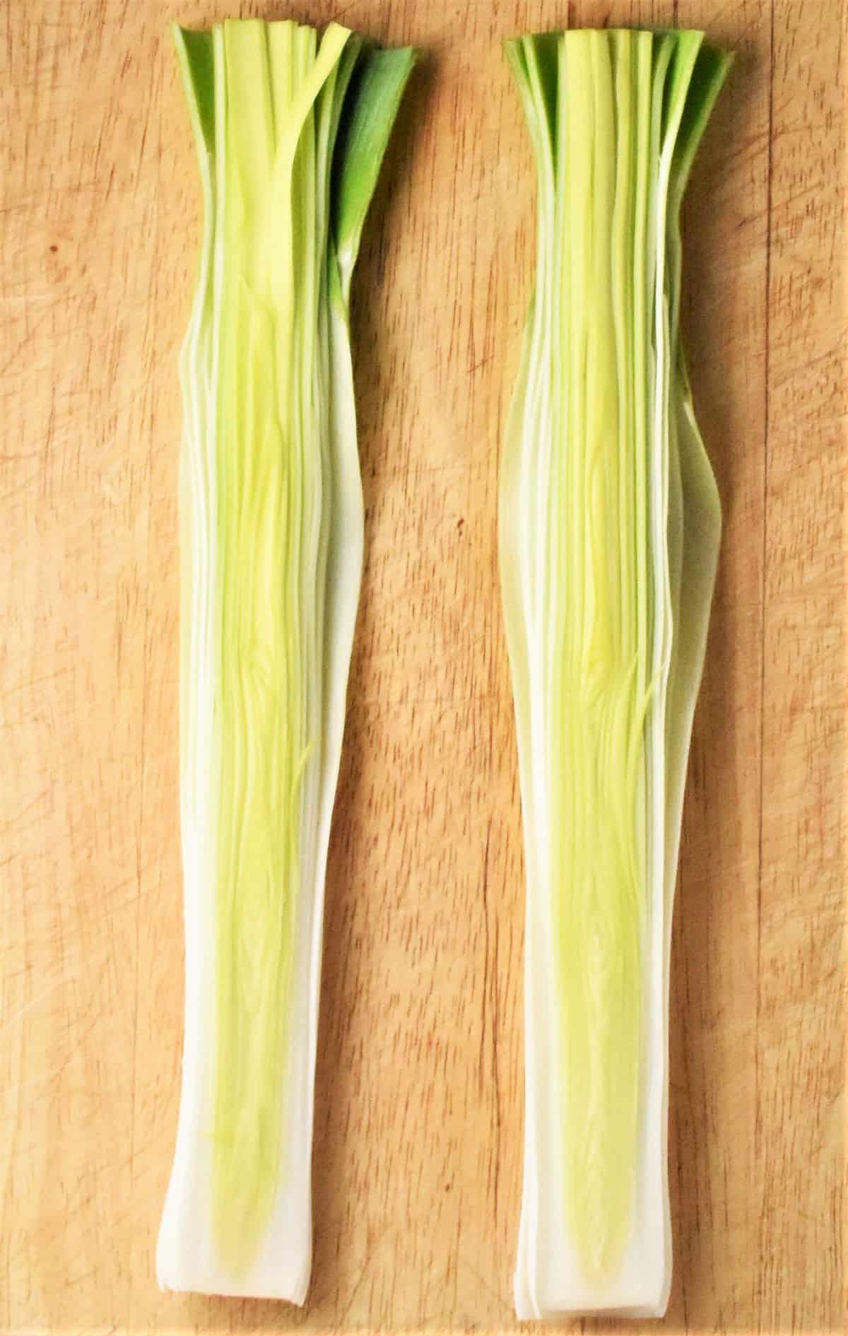 Leek sliced in half lengthways on top of wooden board.