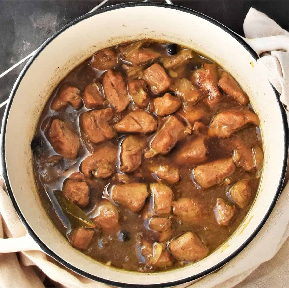 Top down view of pieces of pork in goulash gravy in white pot.