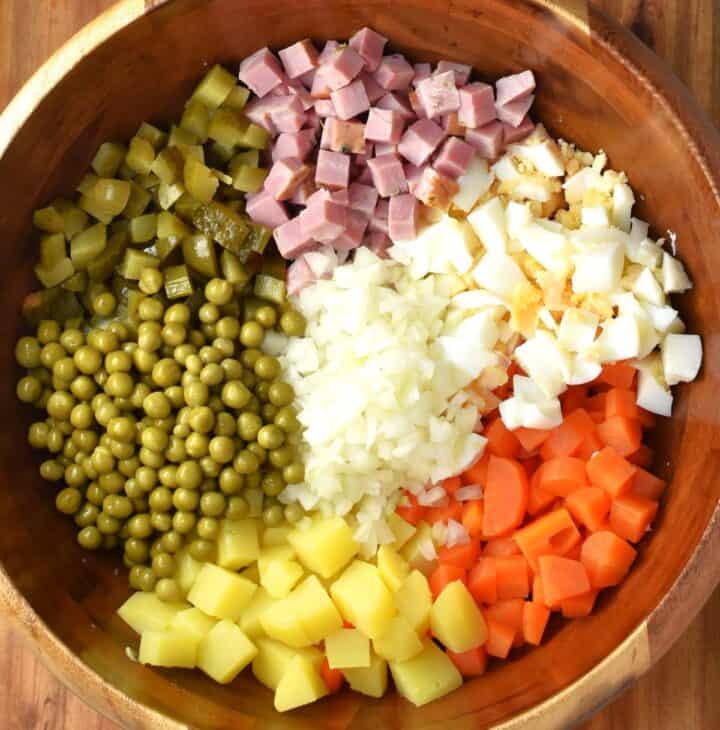 Top down view of chopped vegetables for Olivier salad in wooden bowl.