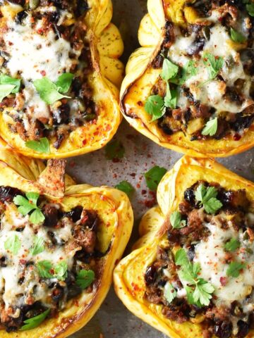 Top down view of 4 sausage stuffed acorn squash with herbs and cheese on top.