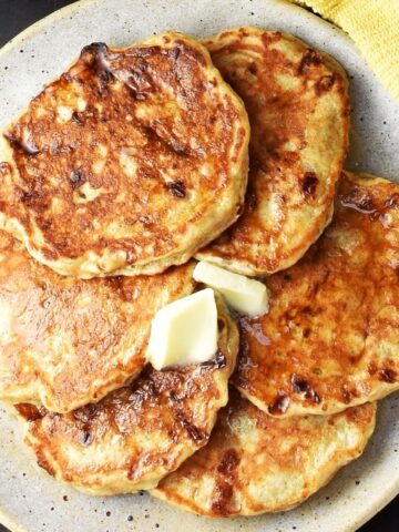 Top down view of cottage cheese banana pancakes with knob of butter on speckled plate.