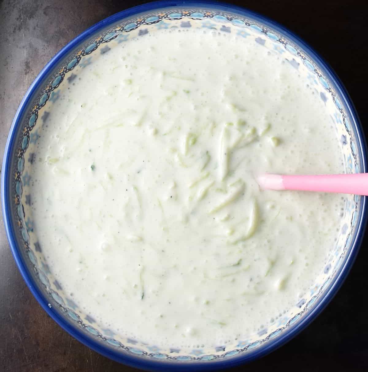 Top down view of cucumber soup with yogurt in blue bowl with pink spoon.